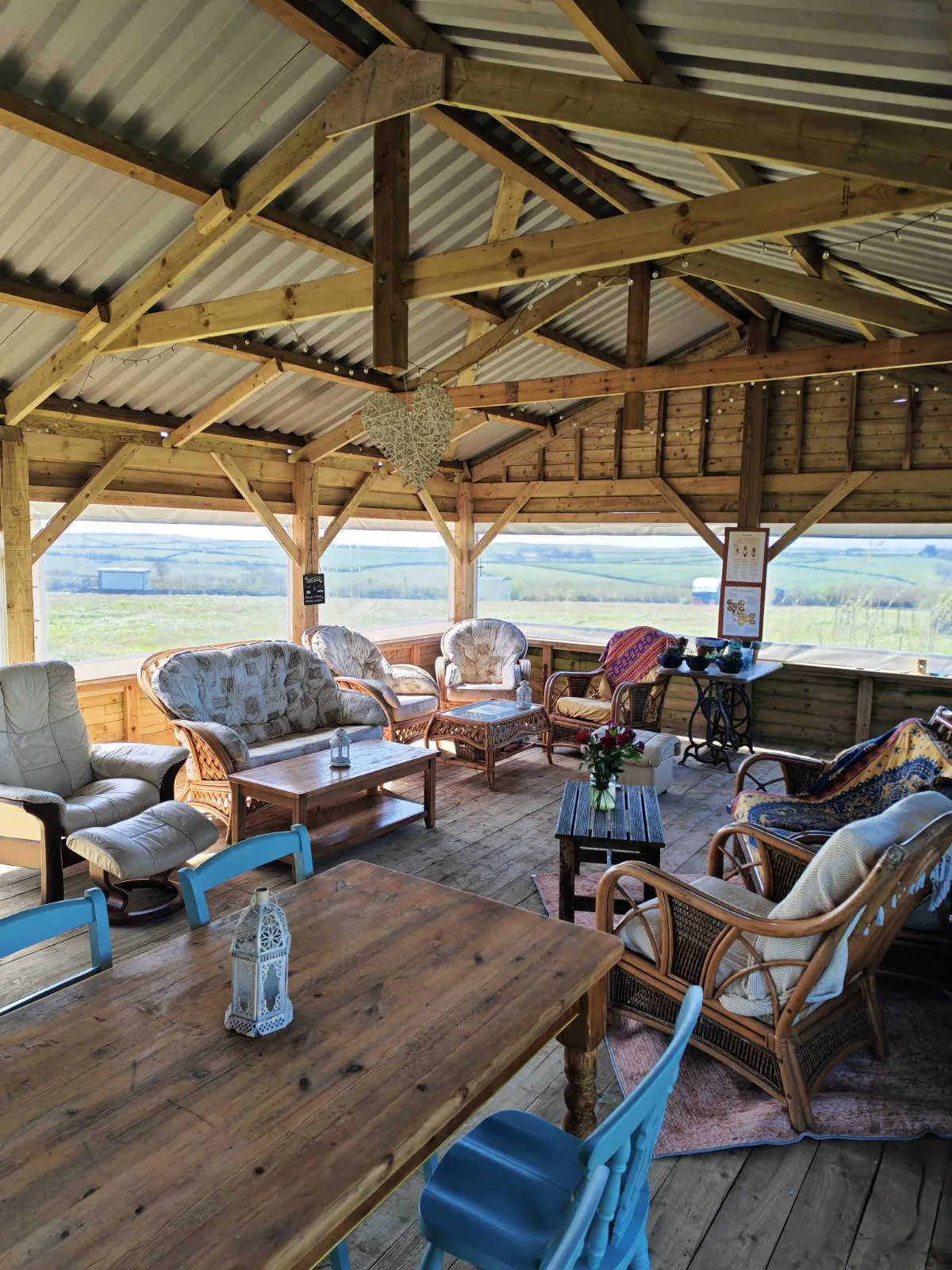 The Coffee Room at West Kellow Yurts: covered open-sided communal space with comfortable seating, a long pine table, and views across the Cornish countryside